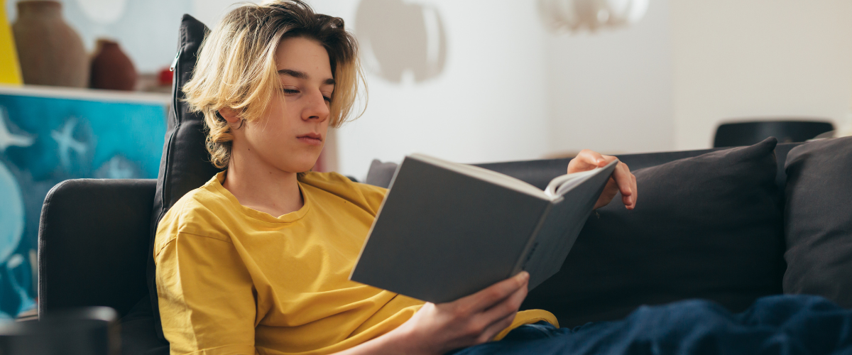 Student laying on a couch reading a book