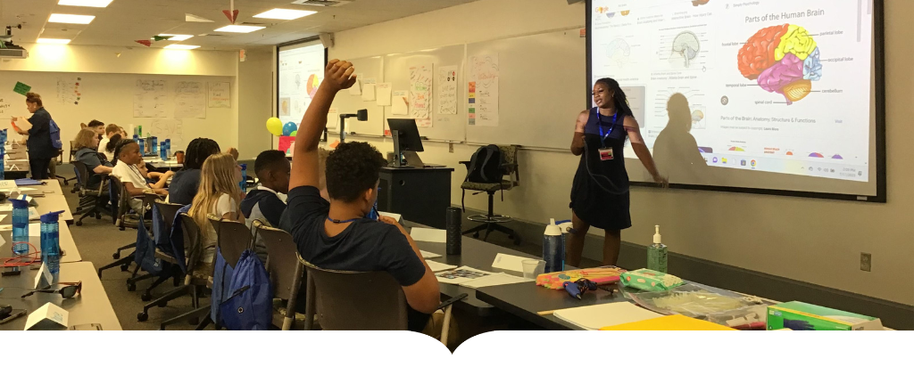 student raises hand as teacher presents